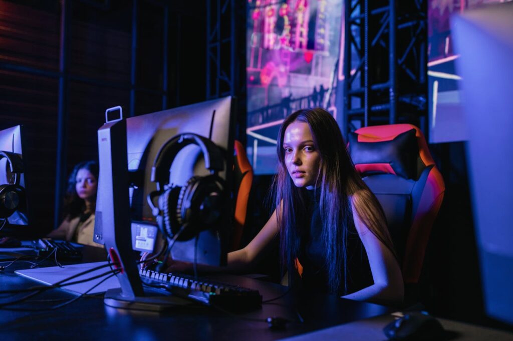 A young woman engages deeply in a video game at an illuminated gaming setup indoors.