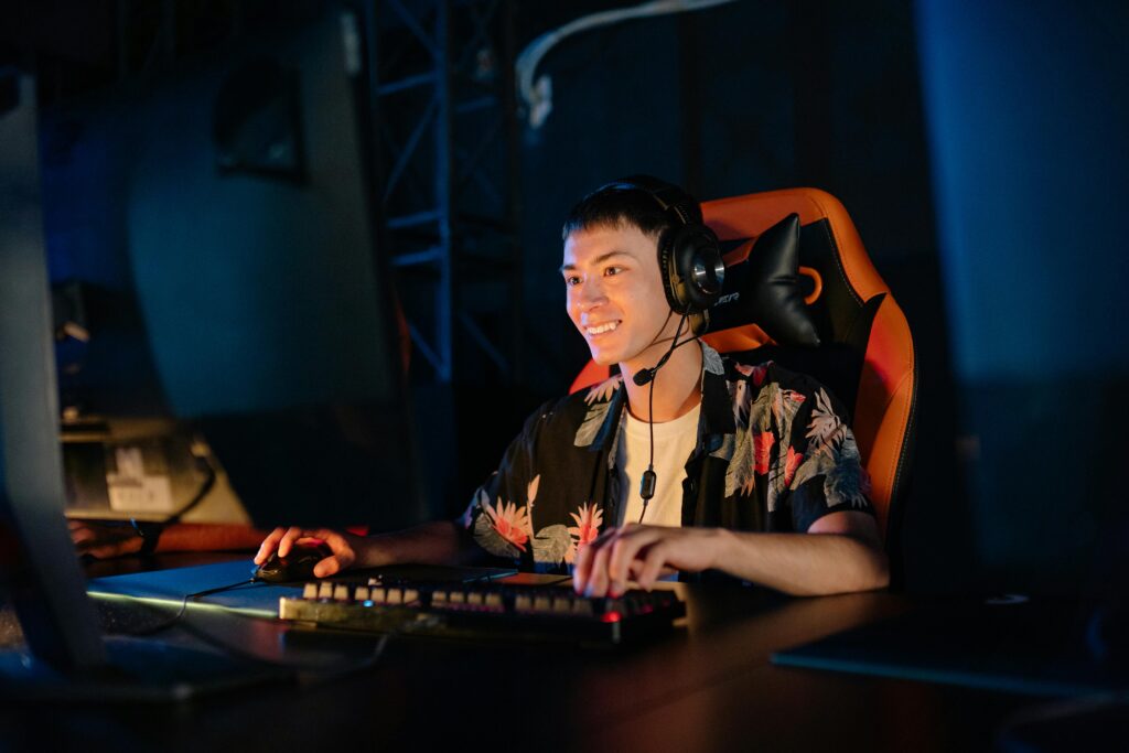 Asian man gaming with headset, keyboard, and mouse. Smiling and focused on screen.